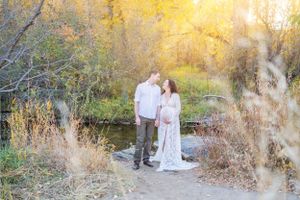 Romantic couple in white attire pose together on a nature path during golden hour.