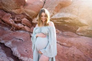 A maternity photo shoot against red rock formations featuring a light blue lace dress and flowing cardigan.