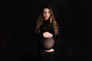 Dramatic maternity portrait in black sheer dress against dark background.