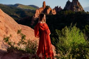 A flowing red dress creates dramatic contrast against the rocky landscape of Garden of the Gods at sunset.