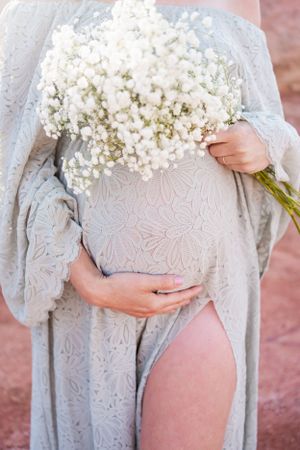 Close-up of baby's breath bouquet held against a light blue lace maternity dress.