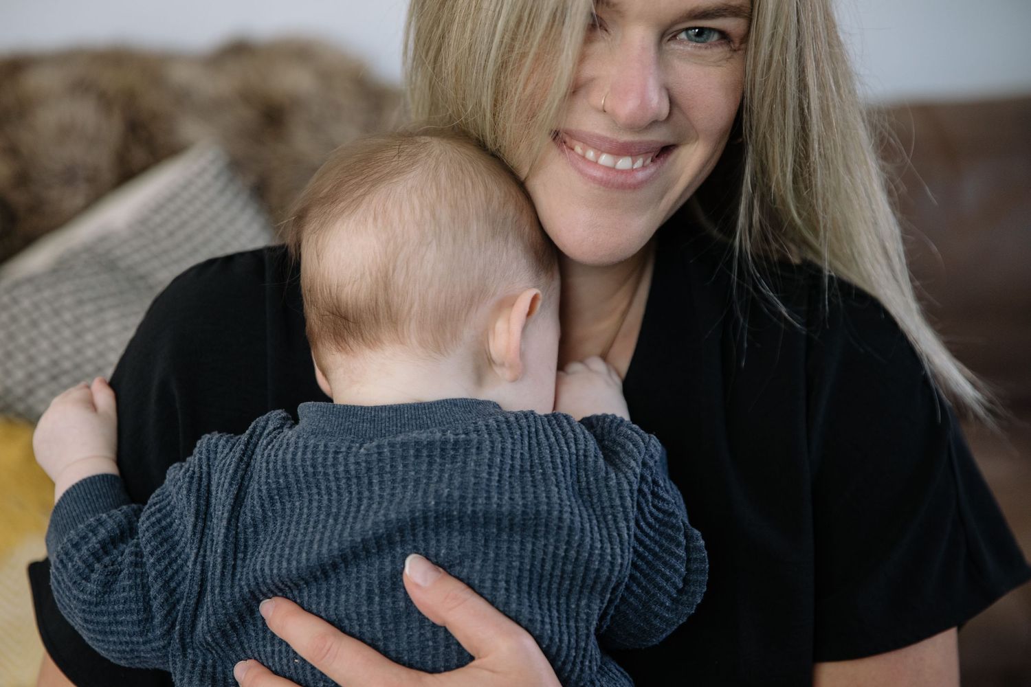 Warm indoor portrait showing loving embrace between caregiver and baby in knit sweater.
