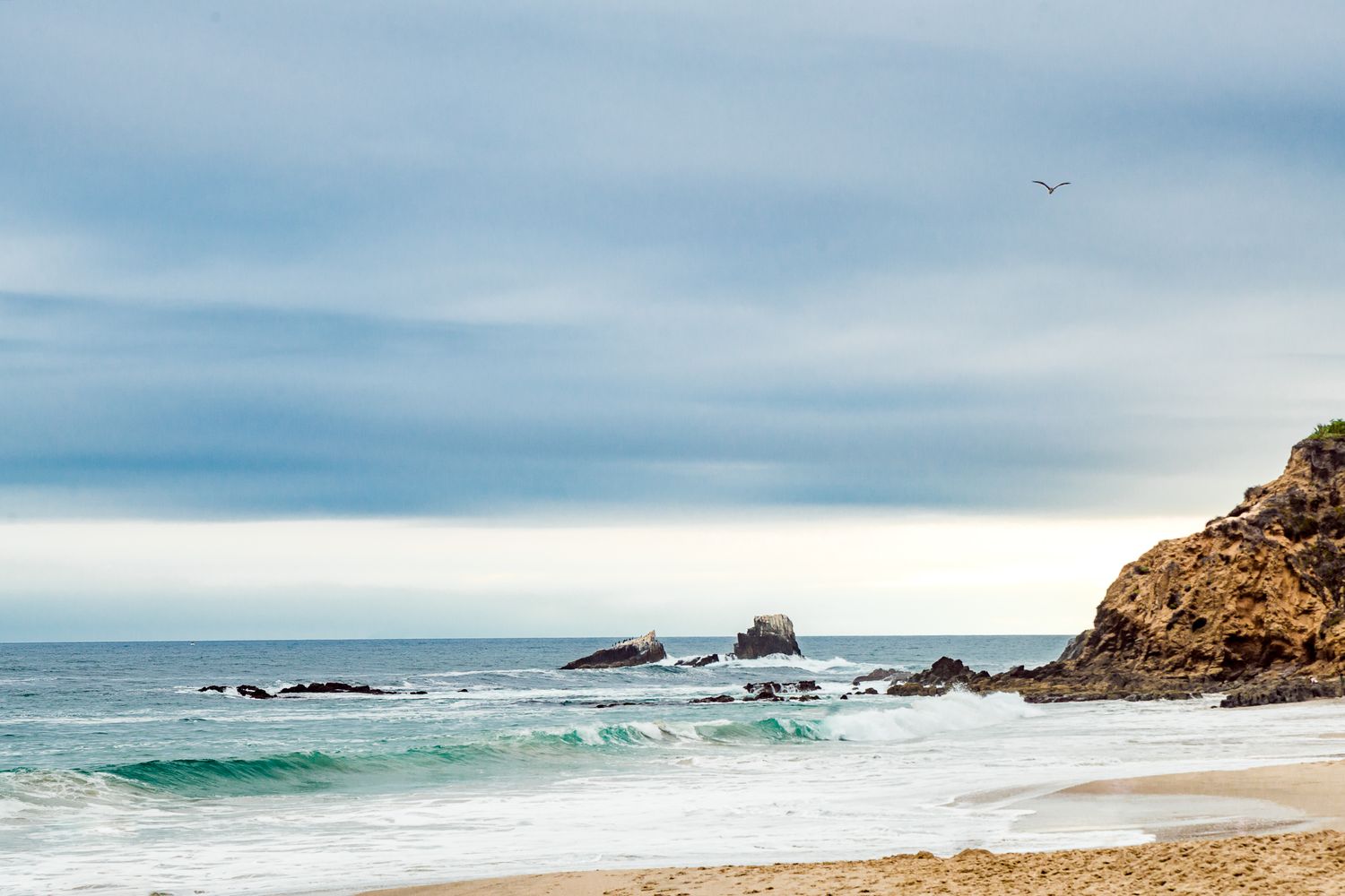 Dramatic coastal landscape with crashing waves, rocky outcrops, and cloudy skies at the beach by Stephanie Coulter Photography