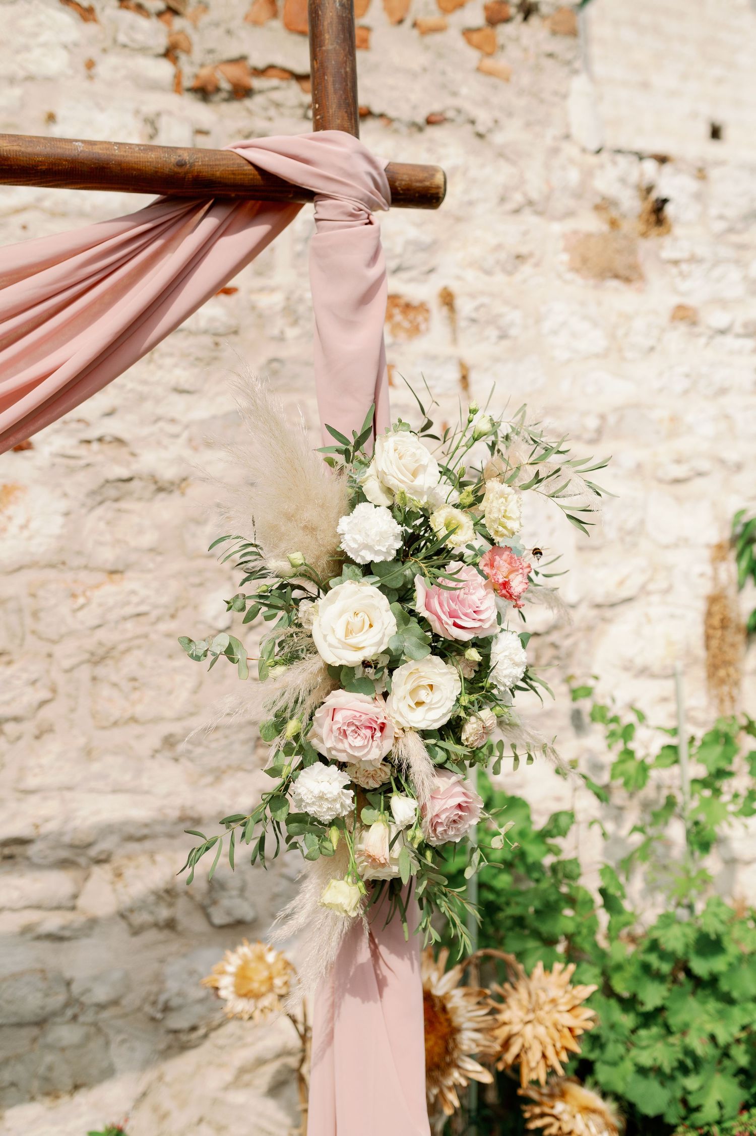 Pink fabric draping decorated with blush and white roses against stone wall.