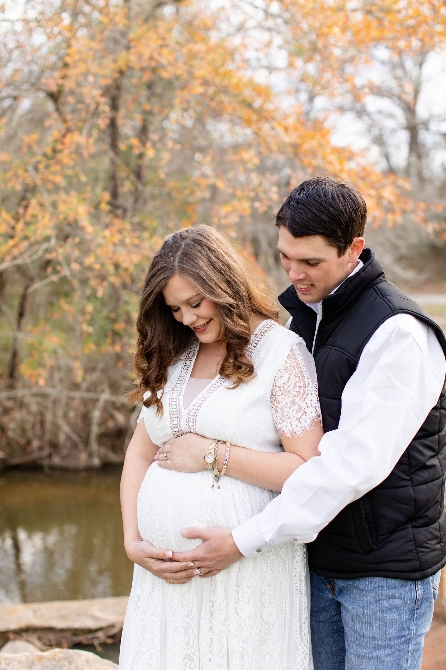 A couple shares an intimate moment by a stream in autumn while wearing white and black clothing.