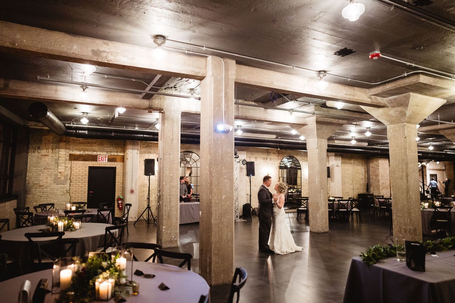 A romantic silhouette of a couple dancing in an industrial-style venue with exposed pillars and dim lighting.