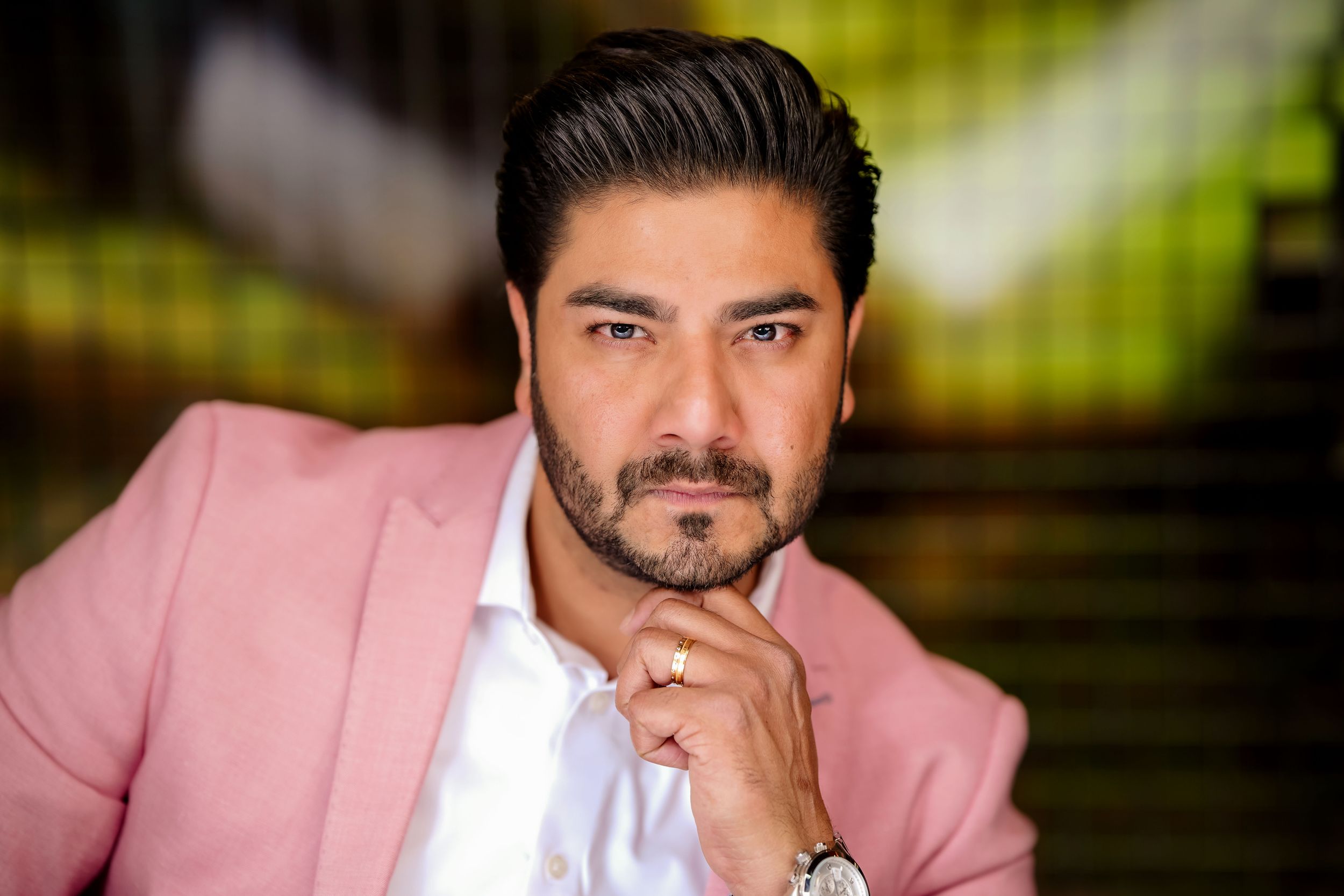 Professional portrait of someone wearing a pink blazer and white shirt with thoughtful pose against blurred background.