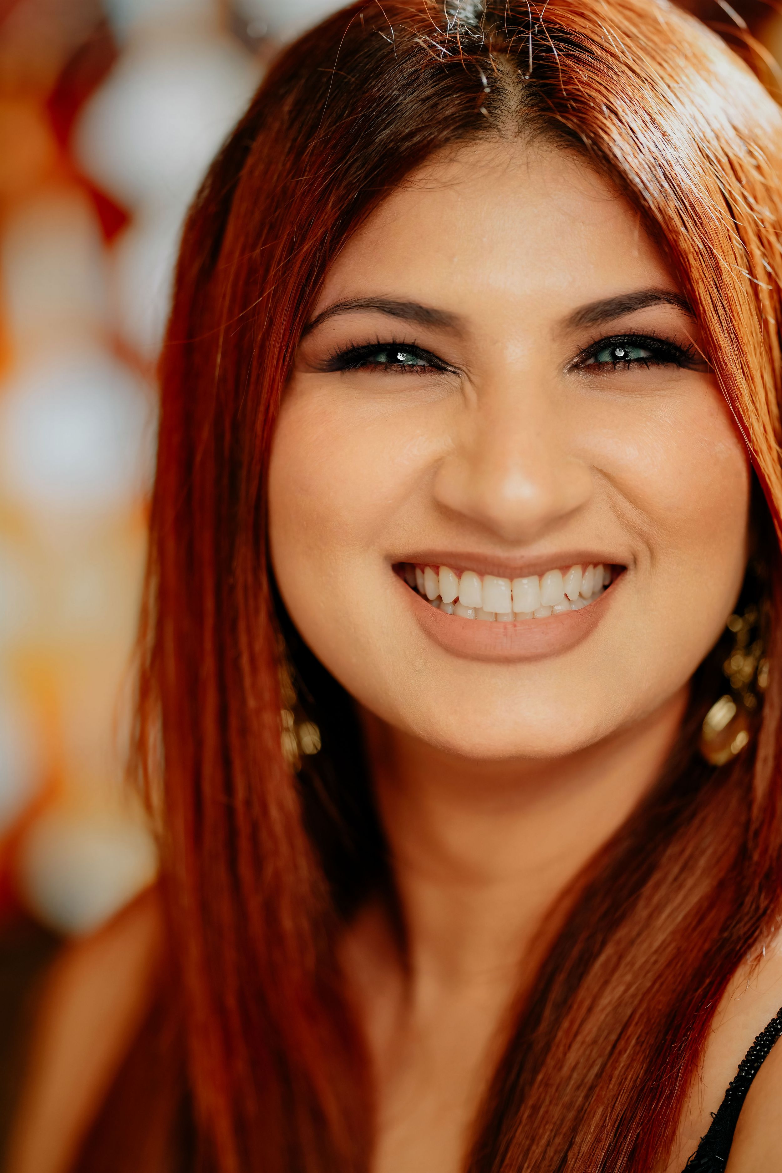 A warm portrait showing a bright smile and vibrant red hair against a soft bokeh background.