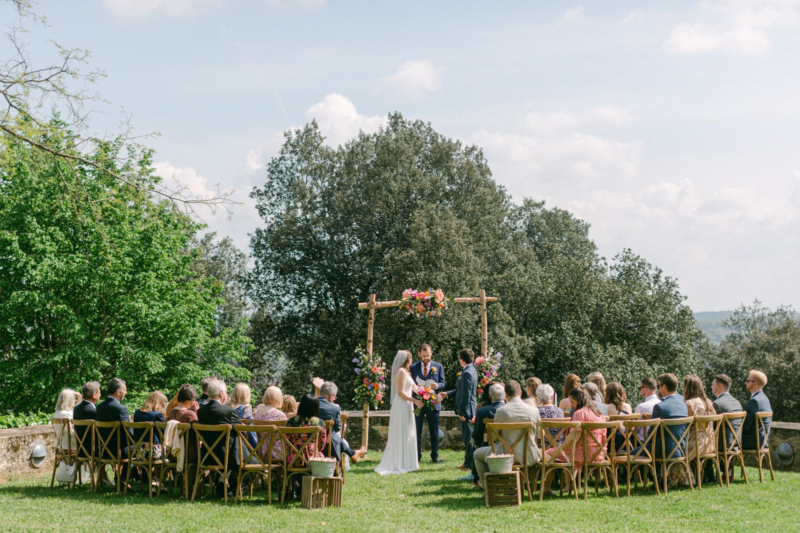 Installation d’une cérémonie de mariage en plein air avec des chaises en bois et une arche fleurie dans un cadre de jardin.