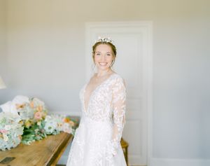 La mariée, portant une élégante robe de mariée en dentelle à manches longues et une couronne délicate, pose en intérieur.