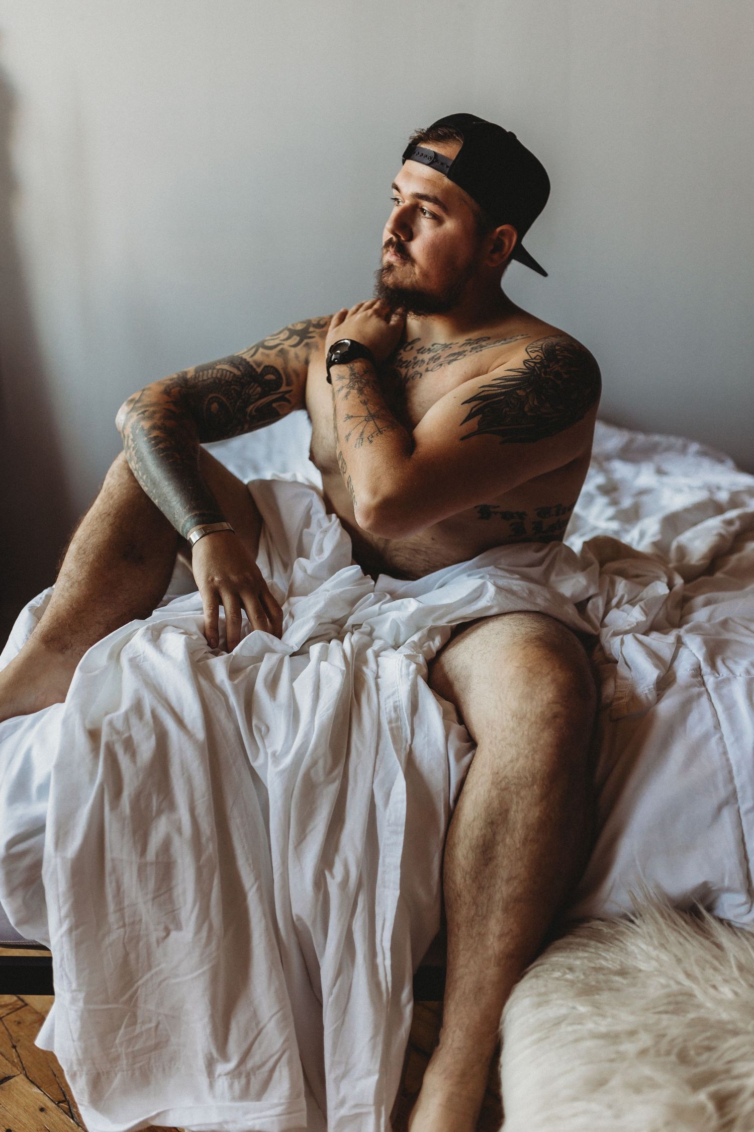 Artistic pose on white bedding with moody natural window light.
