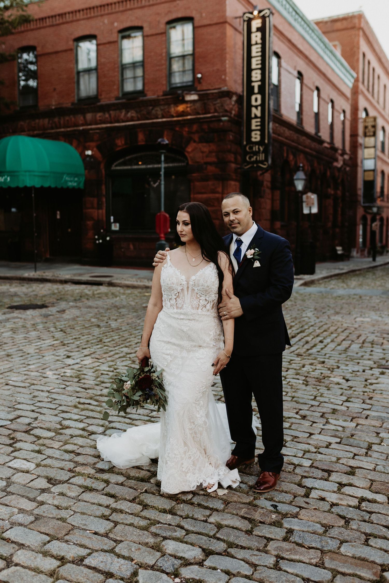 Bride and groom posing on cobblestone street in front of historic brick building. New Bedford, Ma Miranda Photo & Co