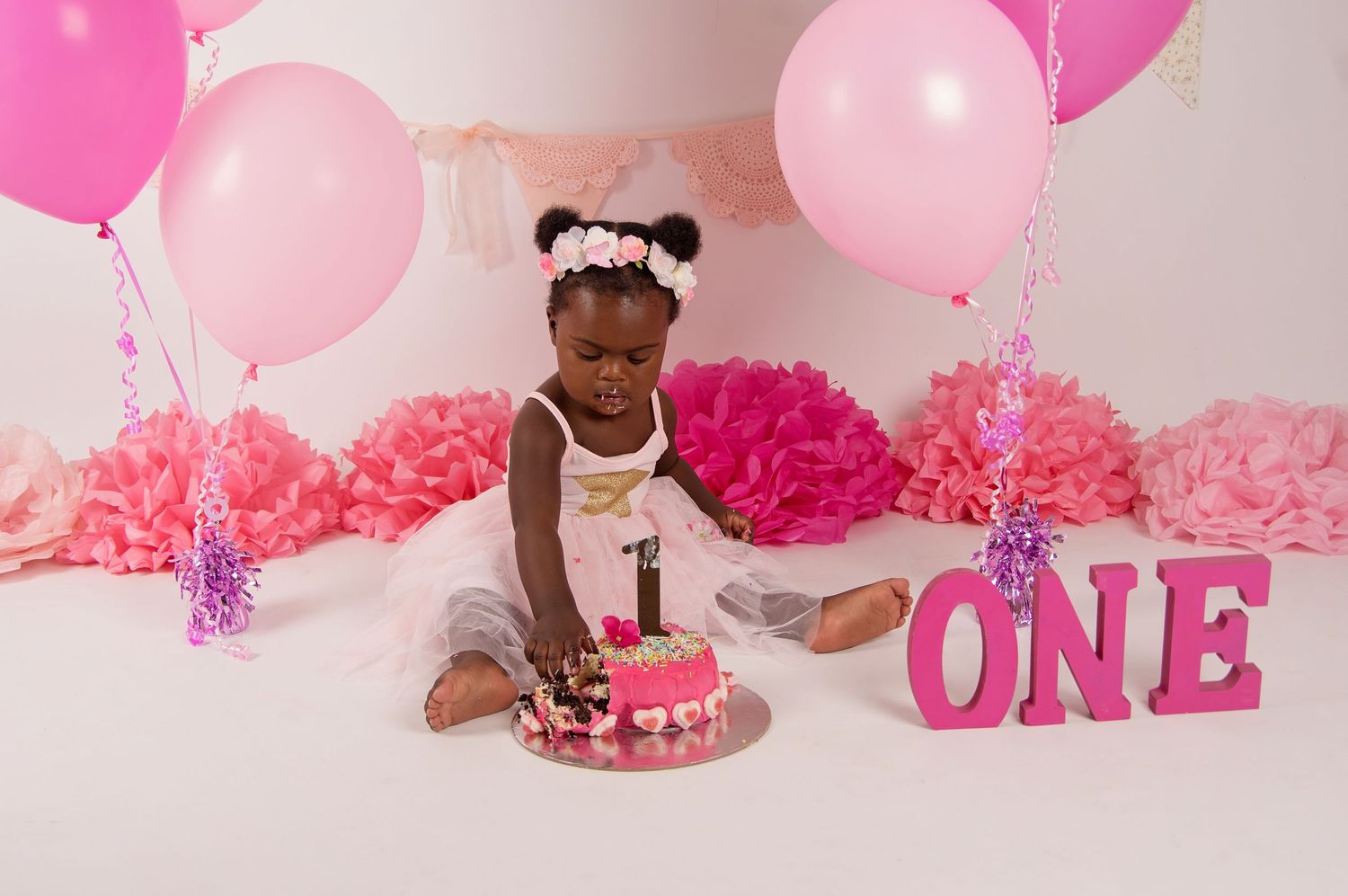 baby girl dressed in pink eating pink cake