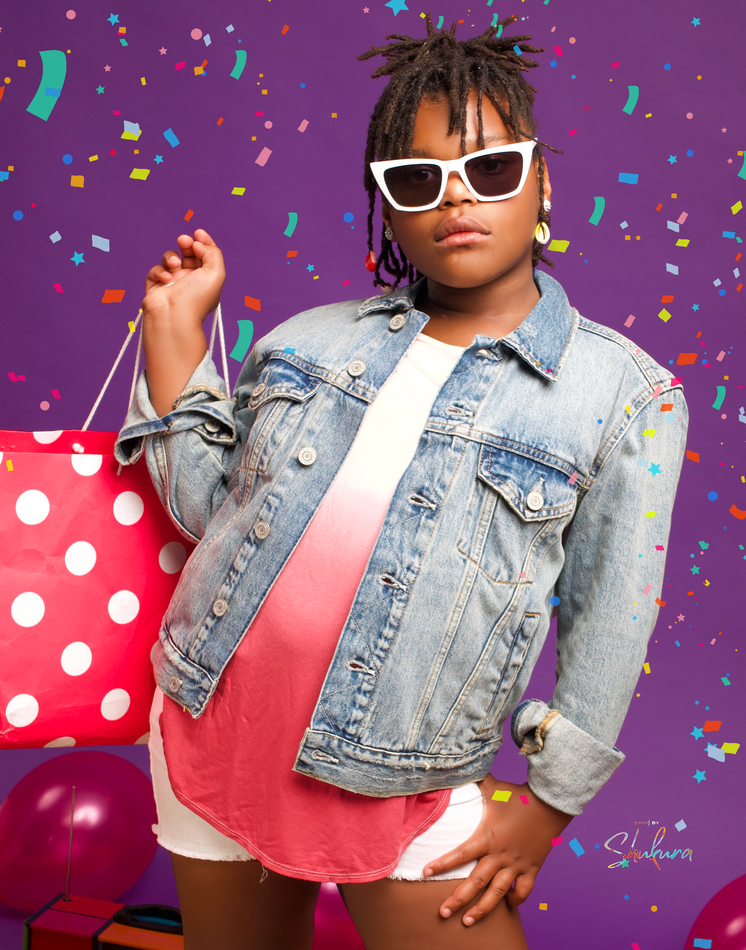 Fun shopping-themed portrait with denim jacket, sunglasses and polka dot shopping bag against purple background.