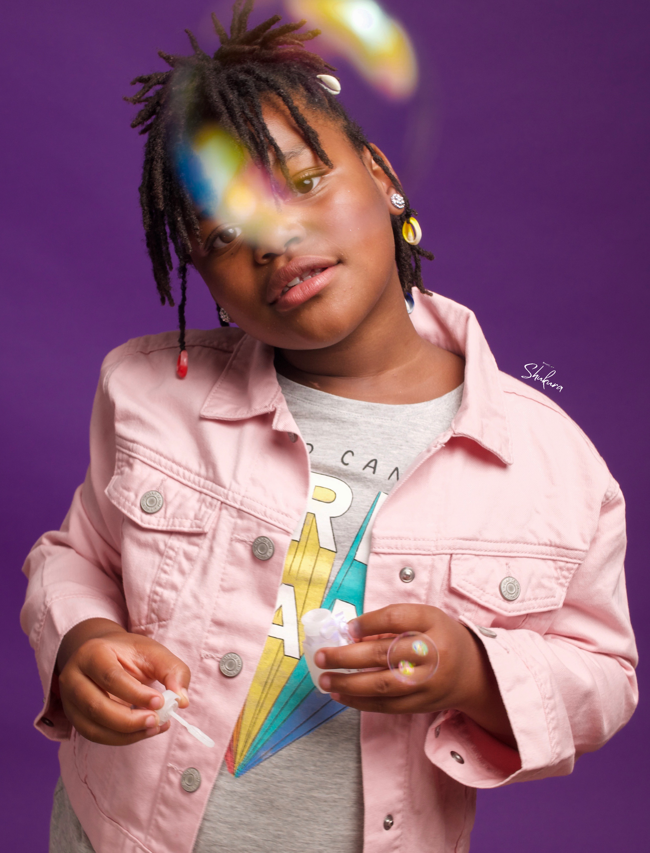 Stylish fashion photo against purple background featuring pink denim jacket and playful lighting effects.