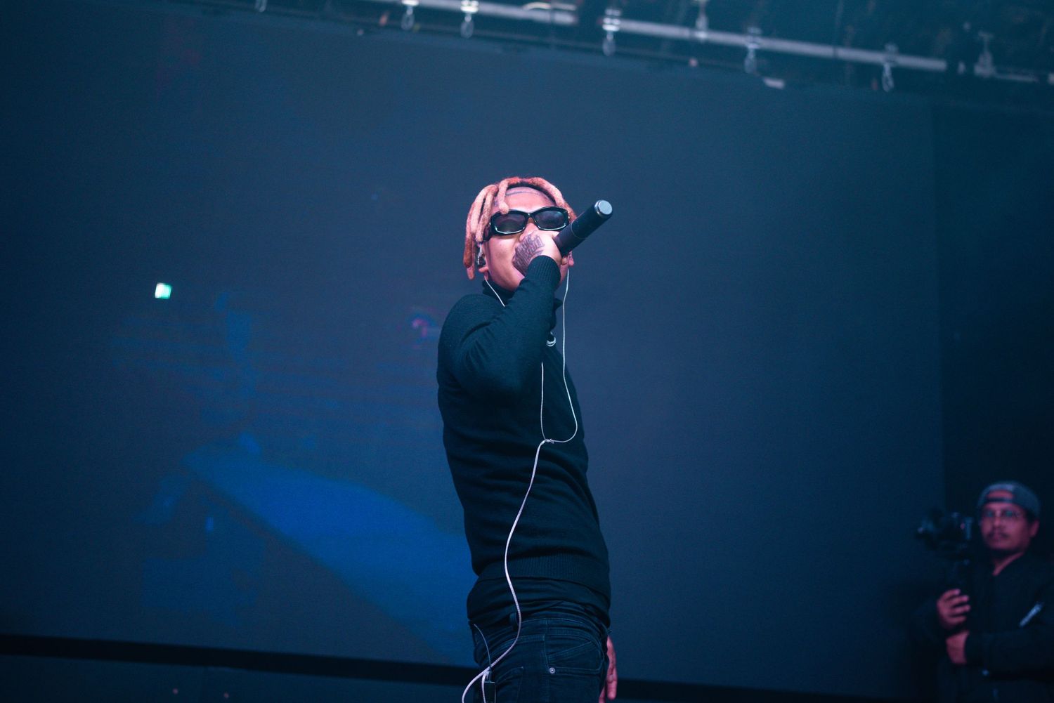 Concert artist in black outfit performing under dramatic stage lighting.