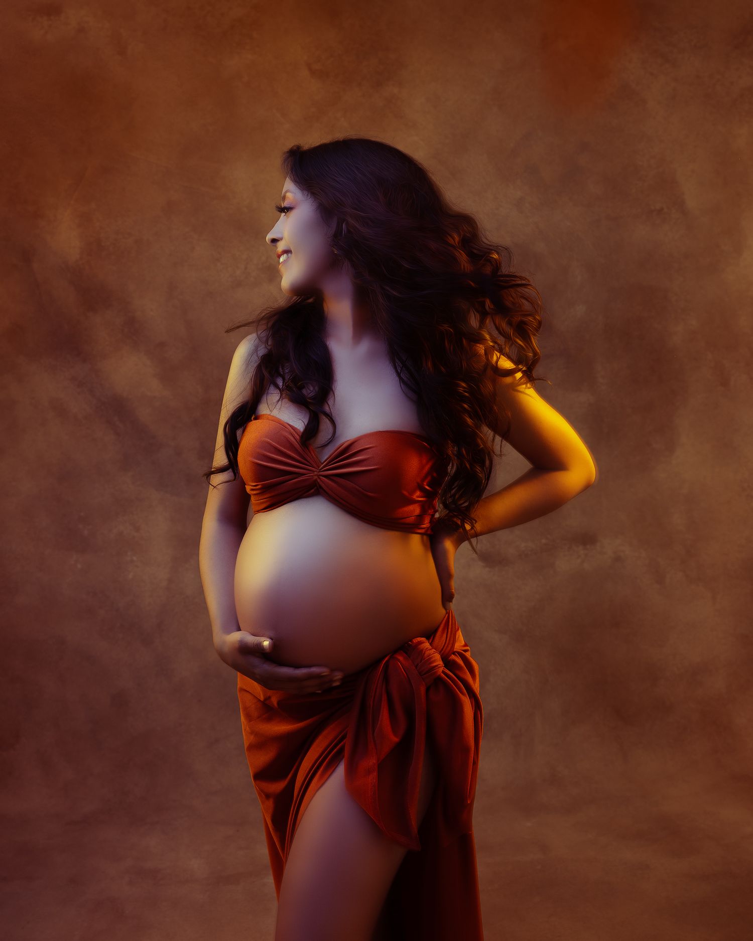 Maternity photography in warm tones showing silhouette against rustic brown backdrop.