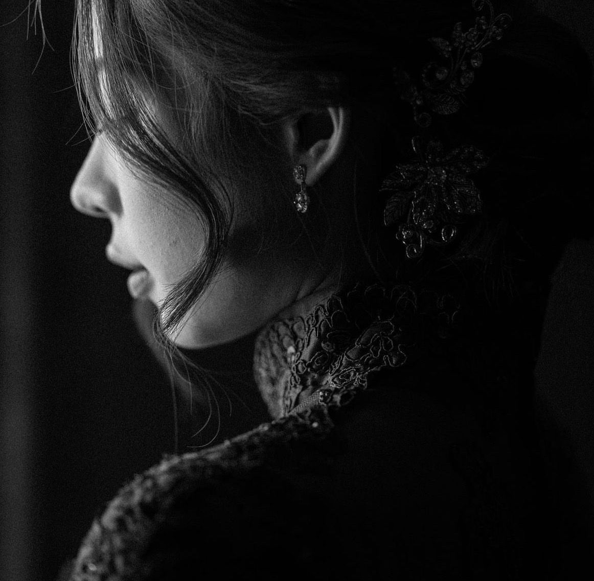 Black and white profile portrait of a woman in elegant lace dress with ornate earring and updo hairstyle.