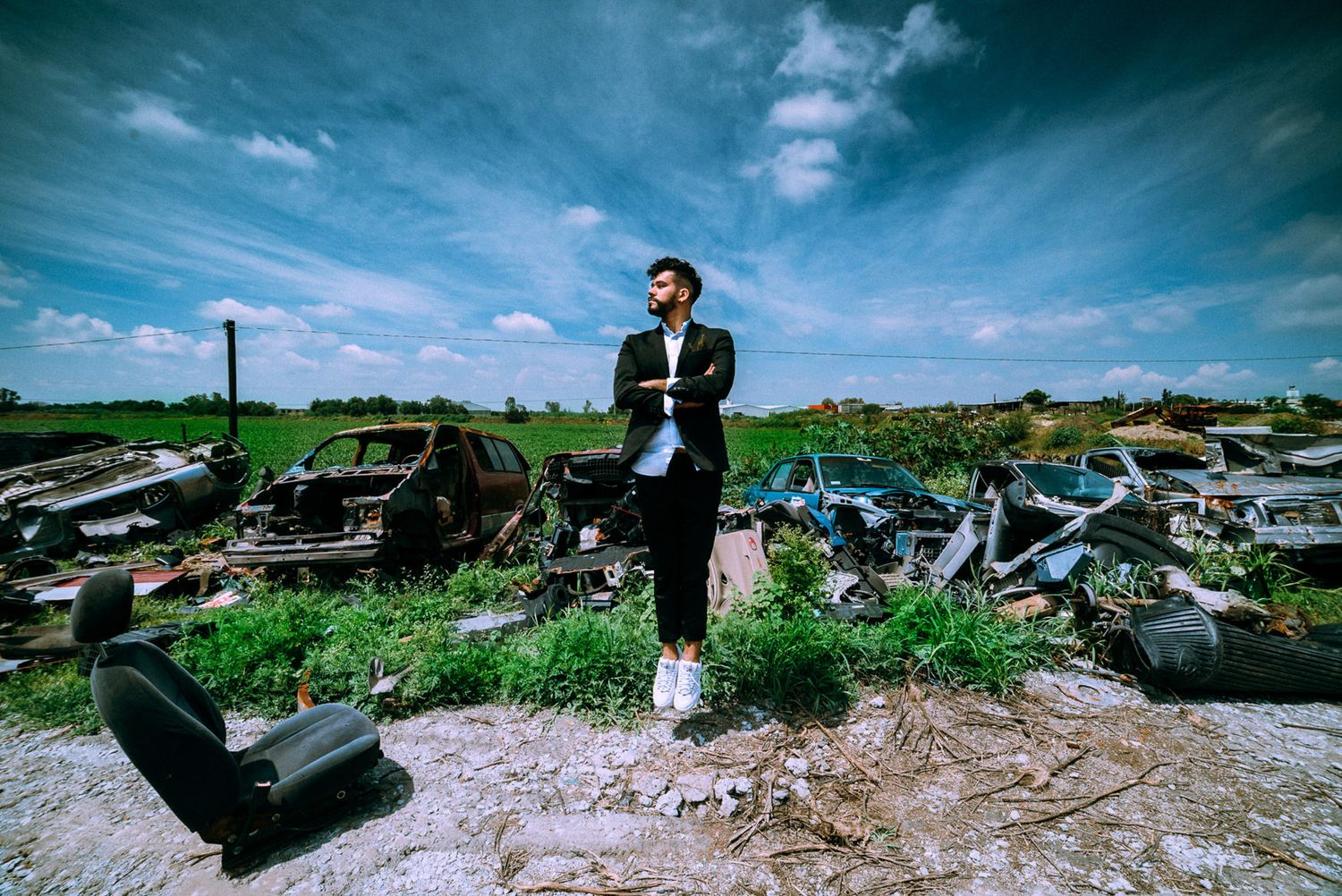 A person in sunglasses stands on a hill overlooking discarded debris and junk under a dramatic blue sky.