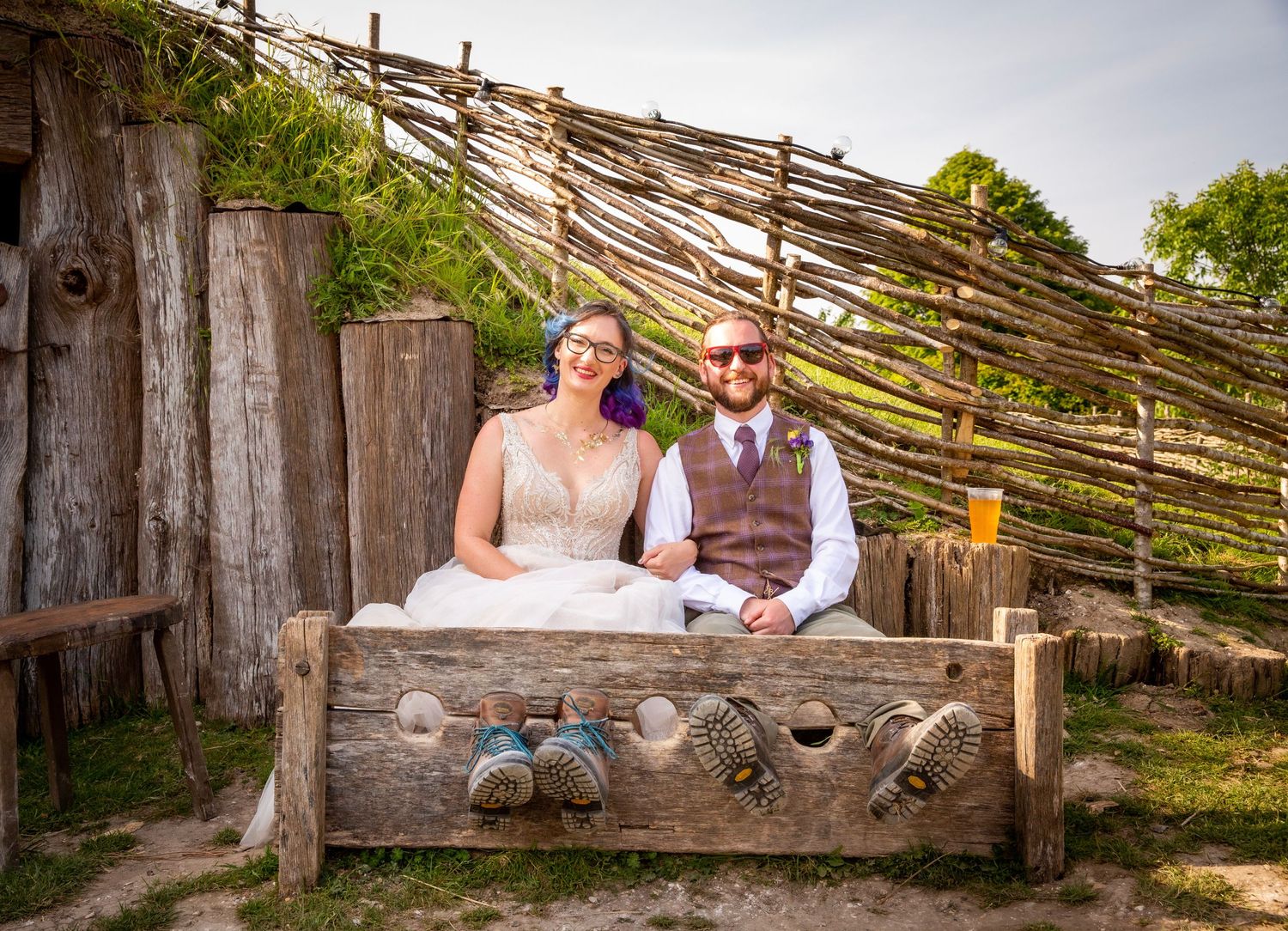 Wedding party relaxes on wooden benches outside a rustic venue.