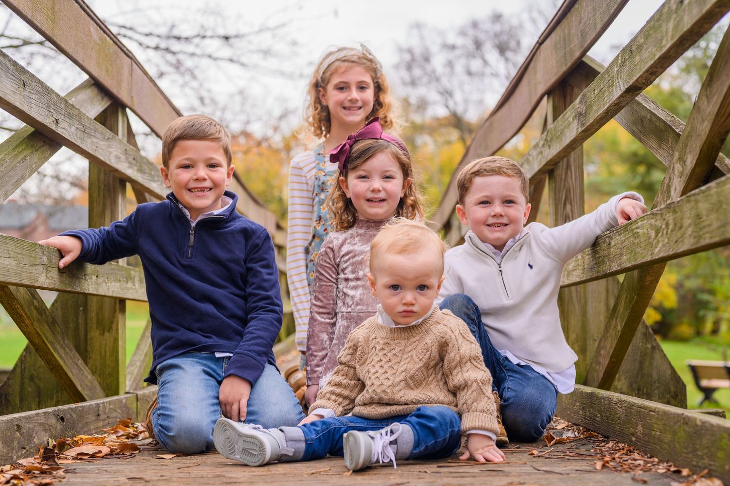 A group of children sitting together on a wooden bridge during an autumn day.