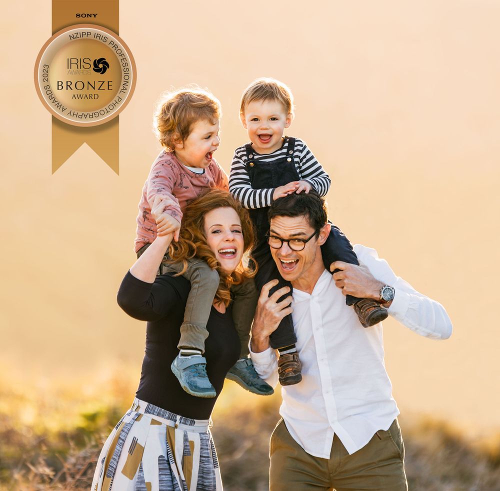 Bronze award winning photo of 2 young boys on shoulders of parents laughing with pink sunlight behind in Christchurch