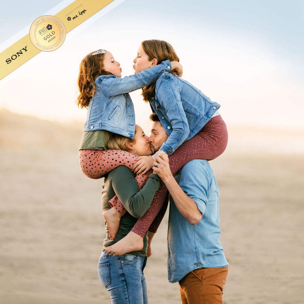 Gold award image of family on beach with daughters on parents shoulders kissing
