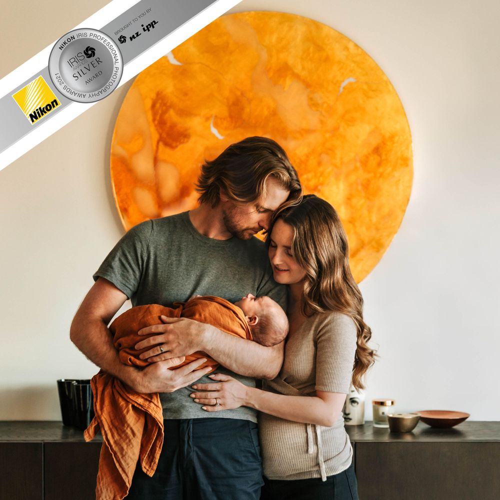 Silver award photo of couple holding a newborn baby swaddled in orange in front of an orange disc wall art Christchurch