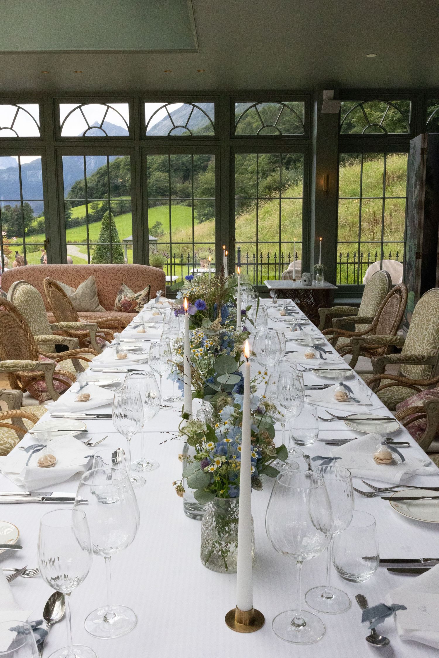 Formal dining table set with white linens and floral centerpiece in a room with panoramic mountain views.
