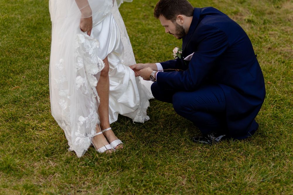 Wedding dress detail shot showing shoes being adjusted on grass.