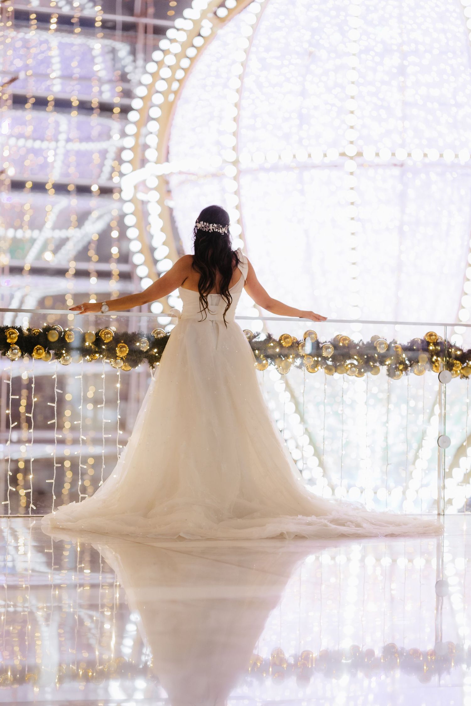 An elegant bride in a ballgown wedding dress stands with arms outstretched before a glittering light display.