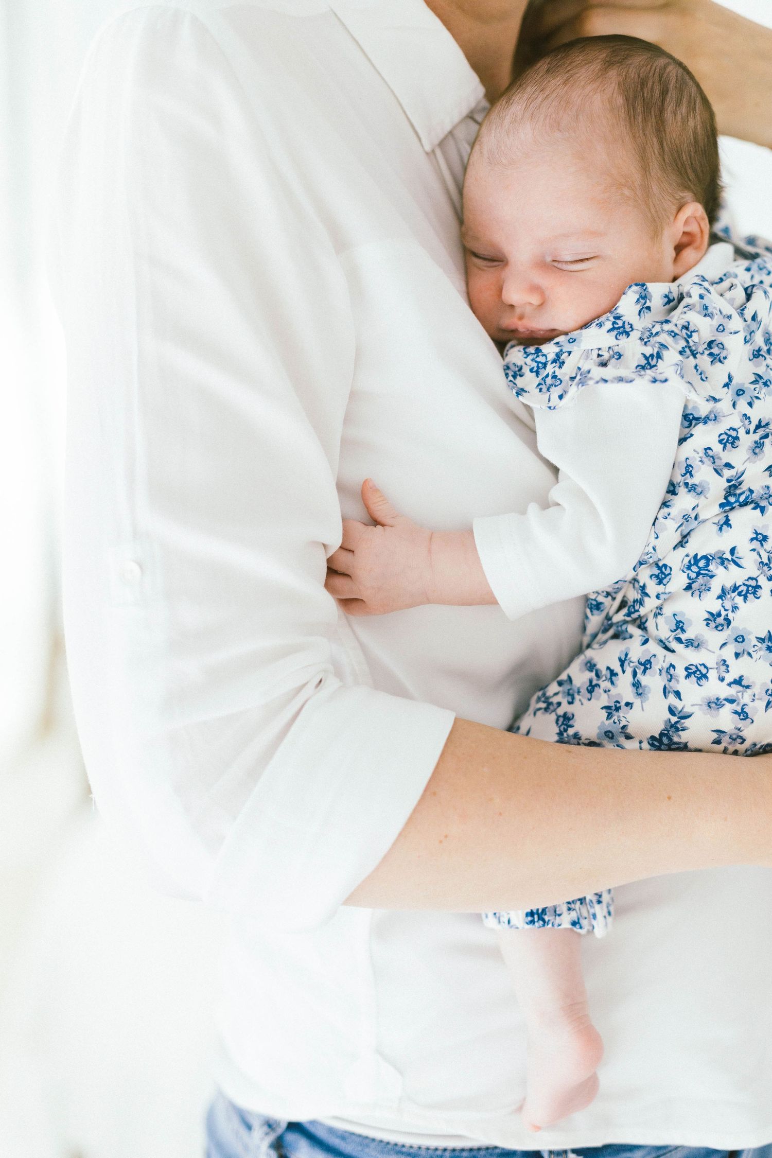 Sleeping newborn in blue floral outfit being held against white background.