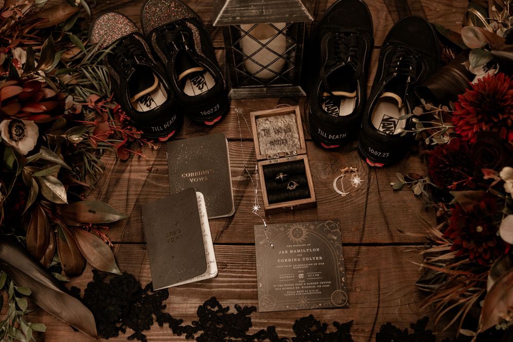 Gothic wedding flat lay with black Vans, dark florals, rings, and celestial-themed invitations.