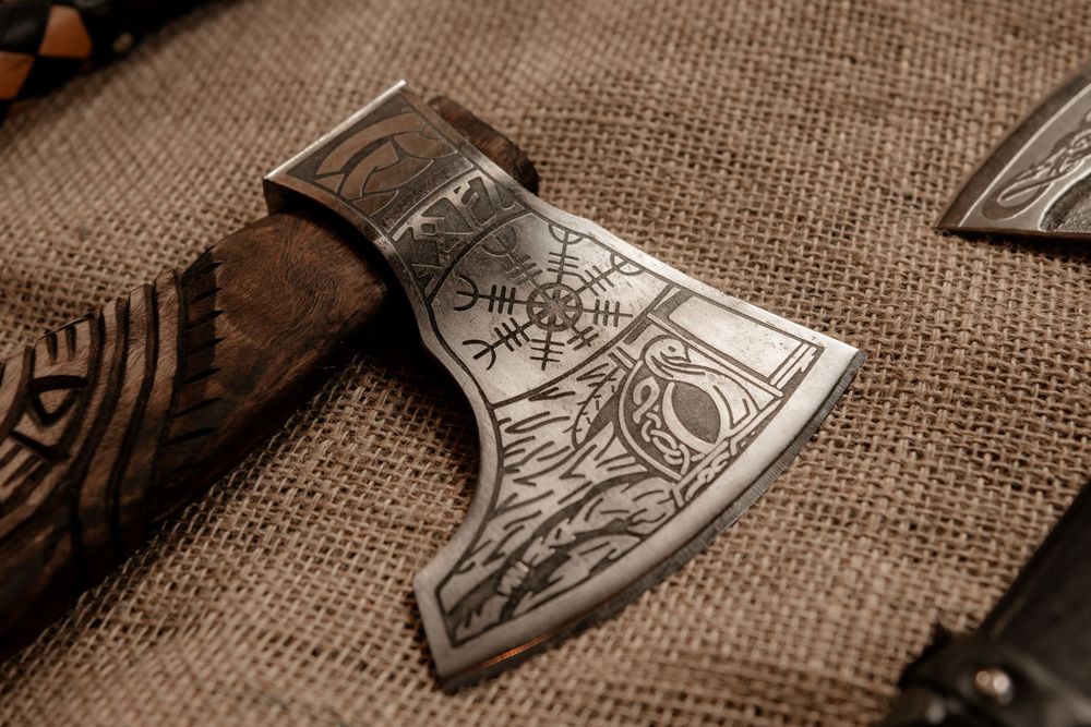 Intricately engraved Viking axe with runic symbols on burlap background for gothic wedding details.
