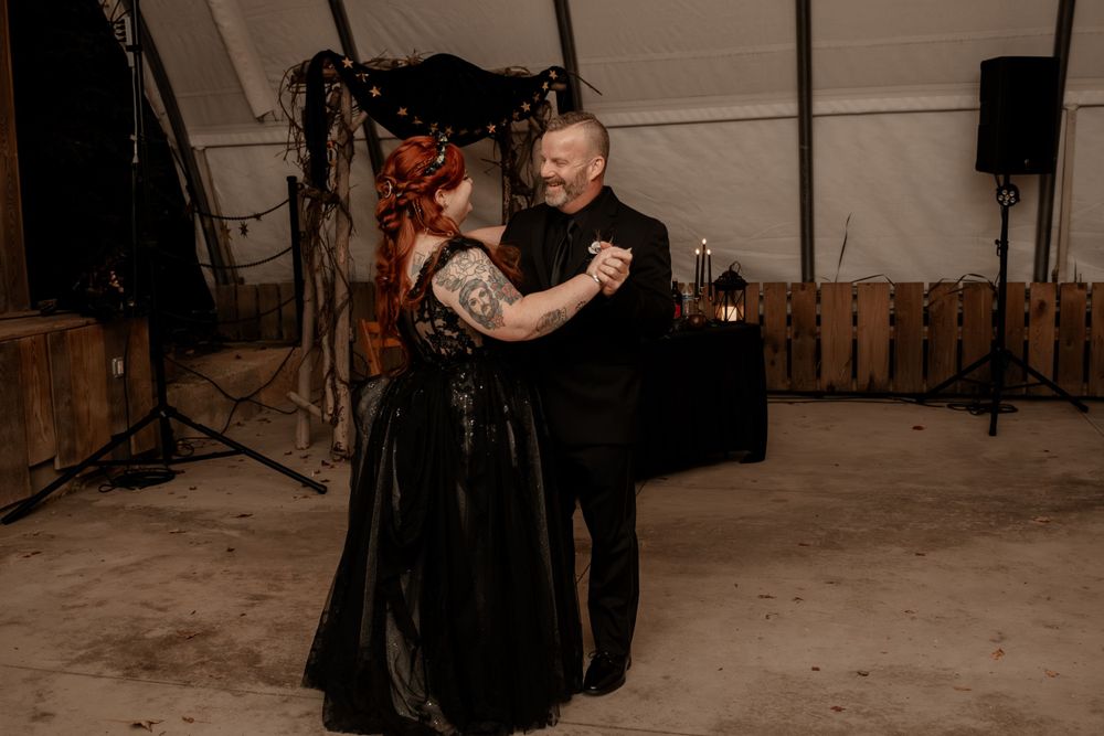 Couple shares first dance in black wedding attire at gothic-themed wedding reception.