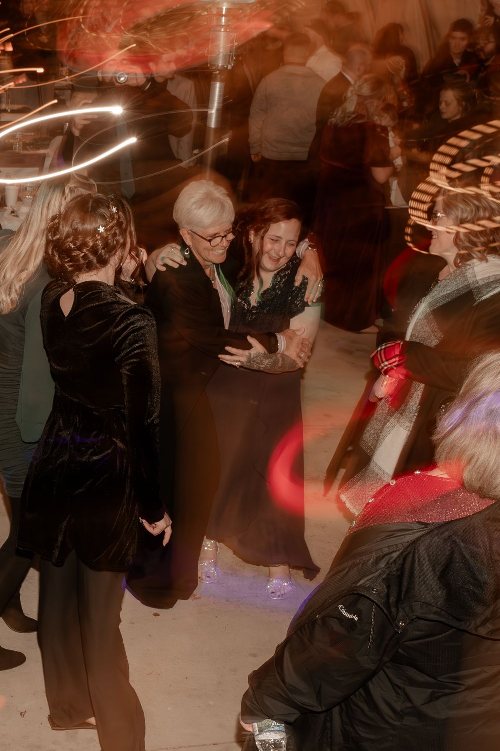 Guests dancing joyfully at a lively wedding reception with colorful light streaks filling the dance floor.