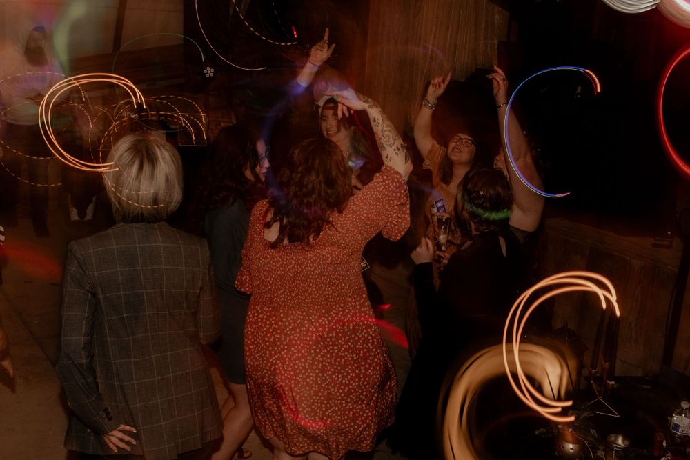 Wedding reception guests dancing energetically with colorful circular light trails captured in long exposure photography.