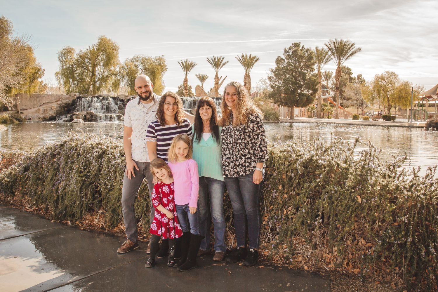 Family gathering posed together by a lake during golden hour with palm trees in background.