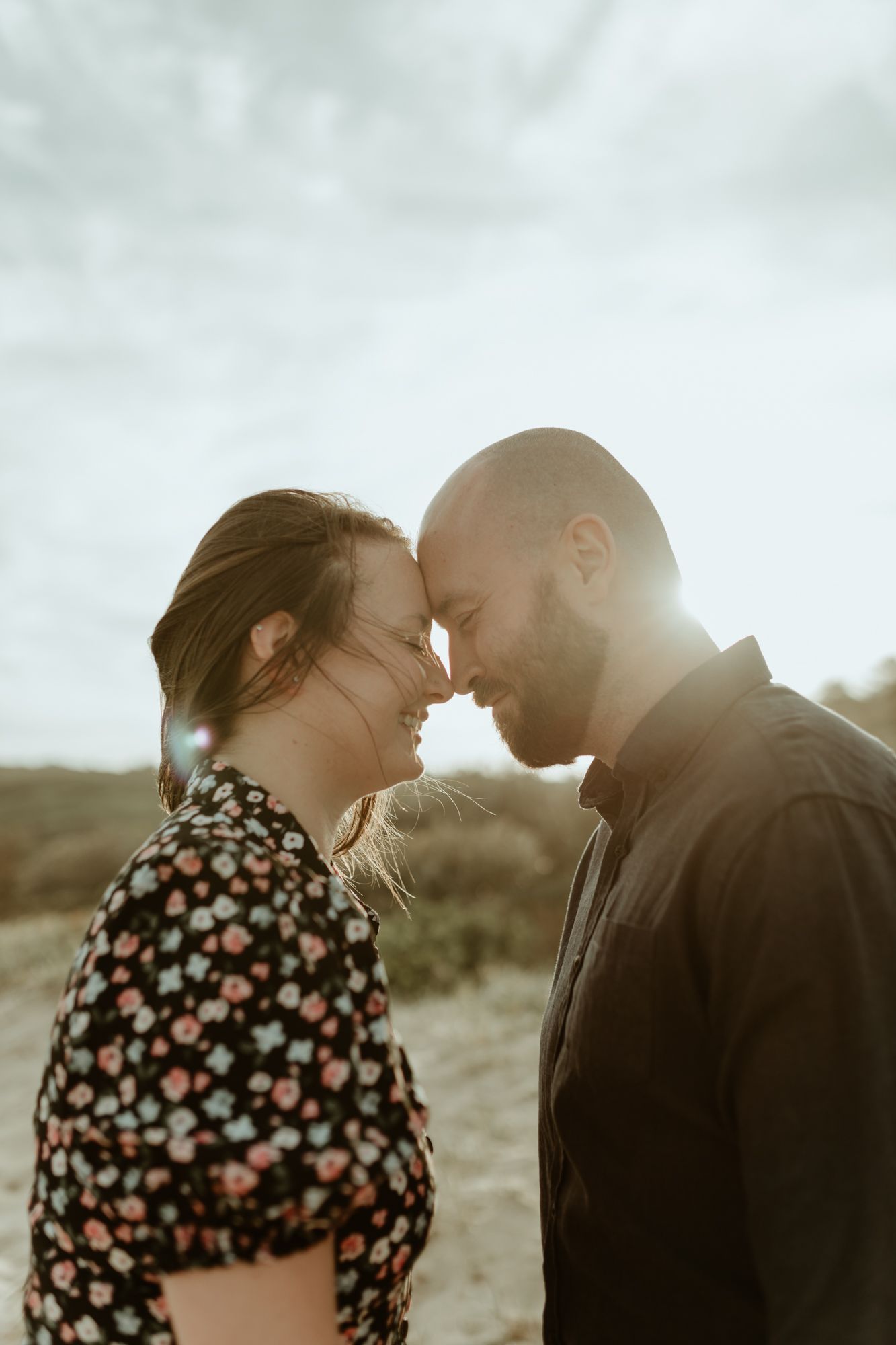 A romantic sunset moment between a couple touching foreheads outdoors with golden light behind them.