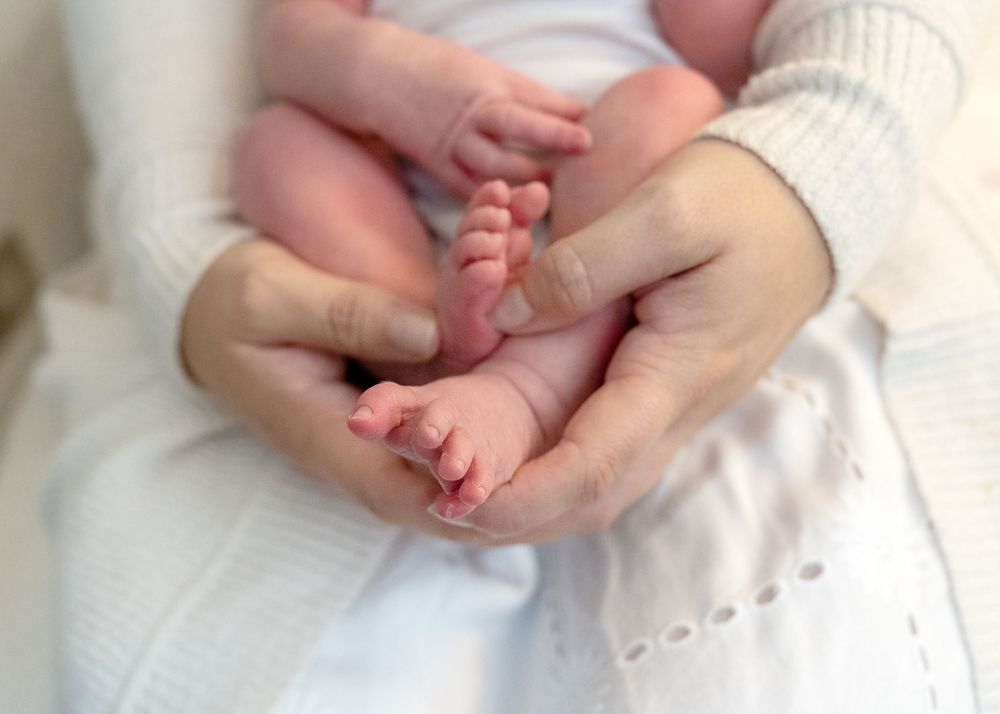 Gentle hands holding tiny newborn baby feet against white fabric.