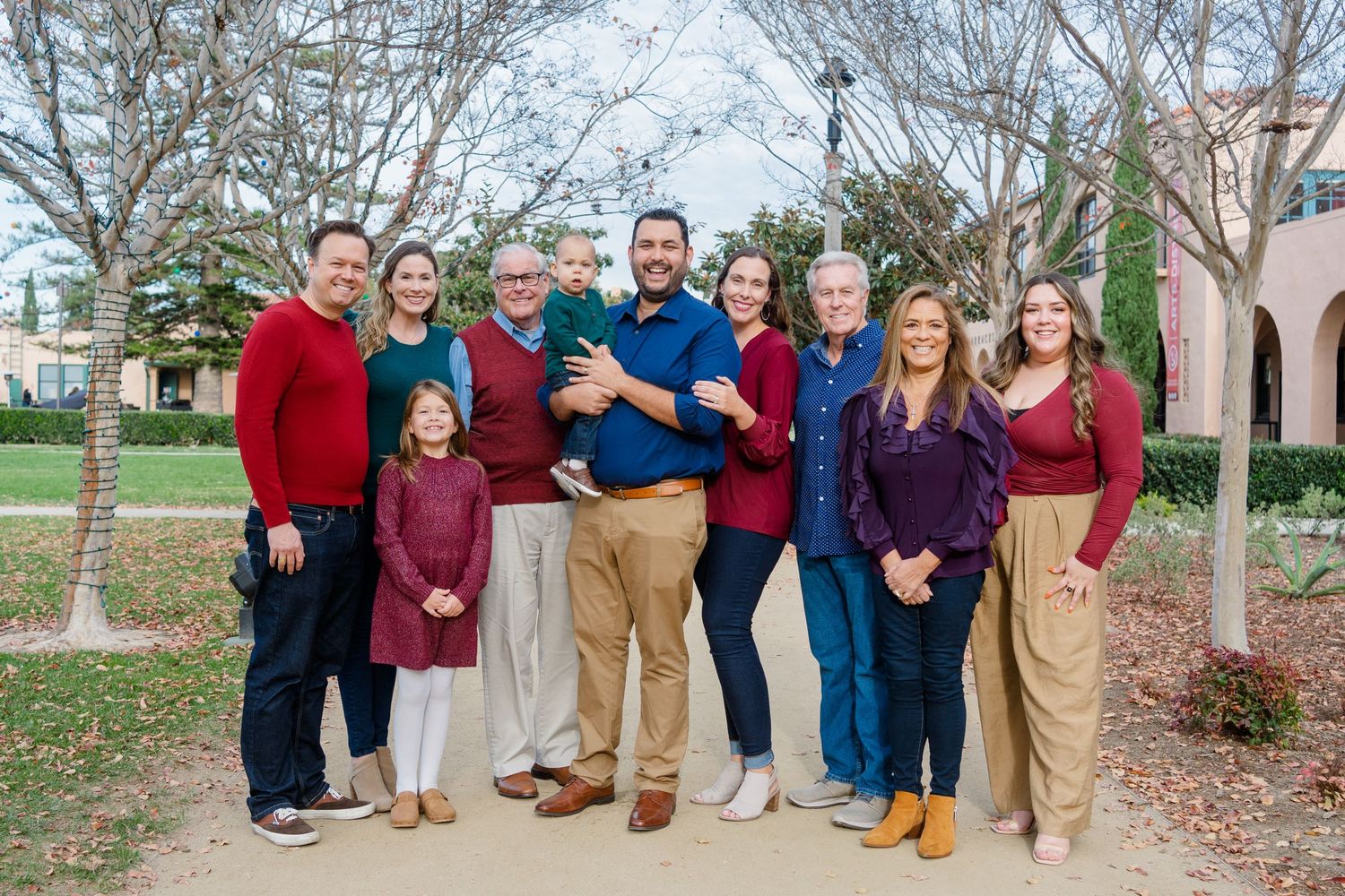 A group of people wearing coordinating red, blue and tan outfits pose together outdoors in front of trees and buildings.