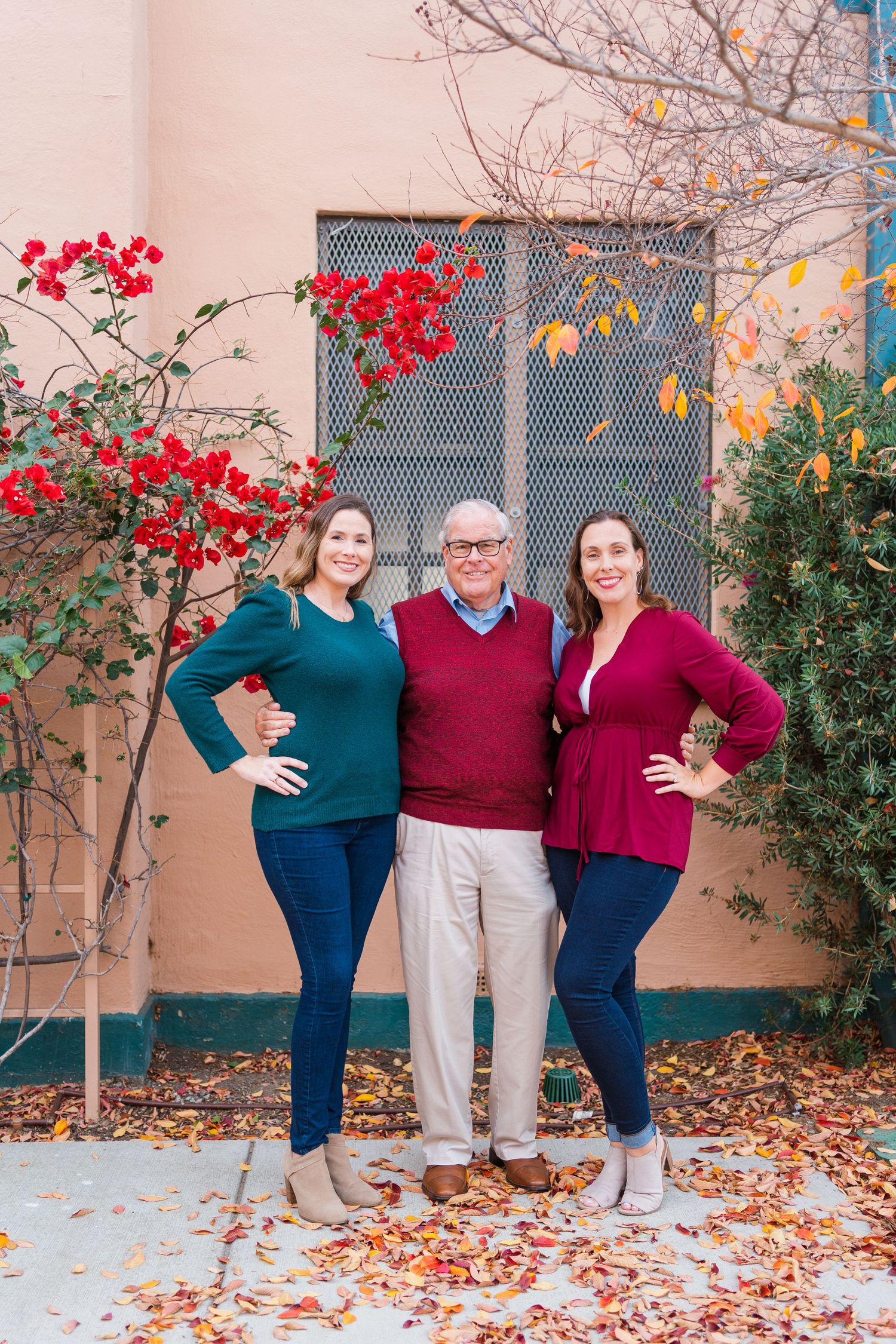 A group posing outdoors in coordinated sweaters with fall leaves on the ground and red berries on branches.