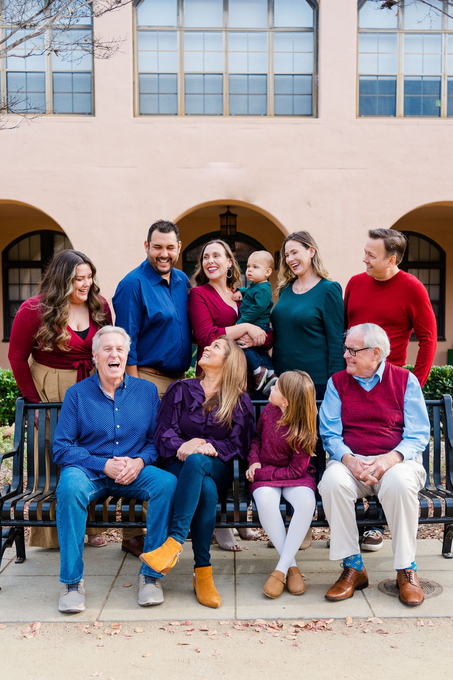 Multi-generational family in coordinating blue, red and burgundy outfits posed together on outdoor bench.