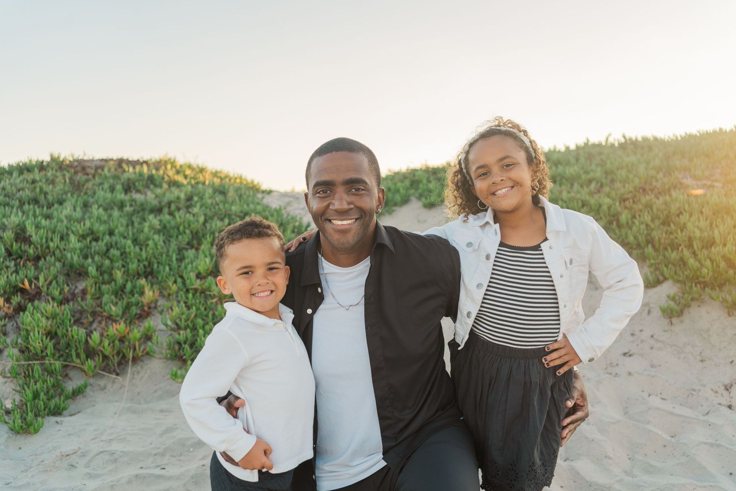 A joyful moment captured at sunset on a sandy beach with flowering plants in the background.