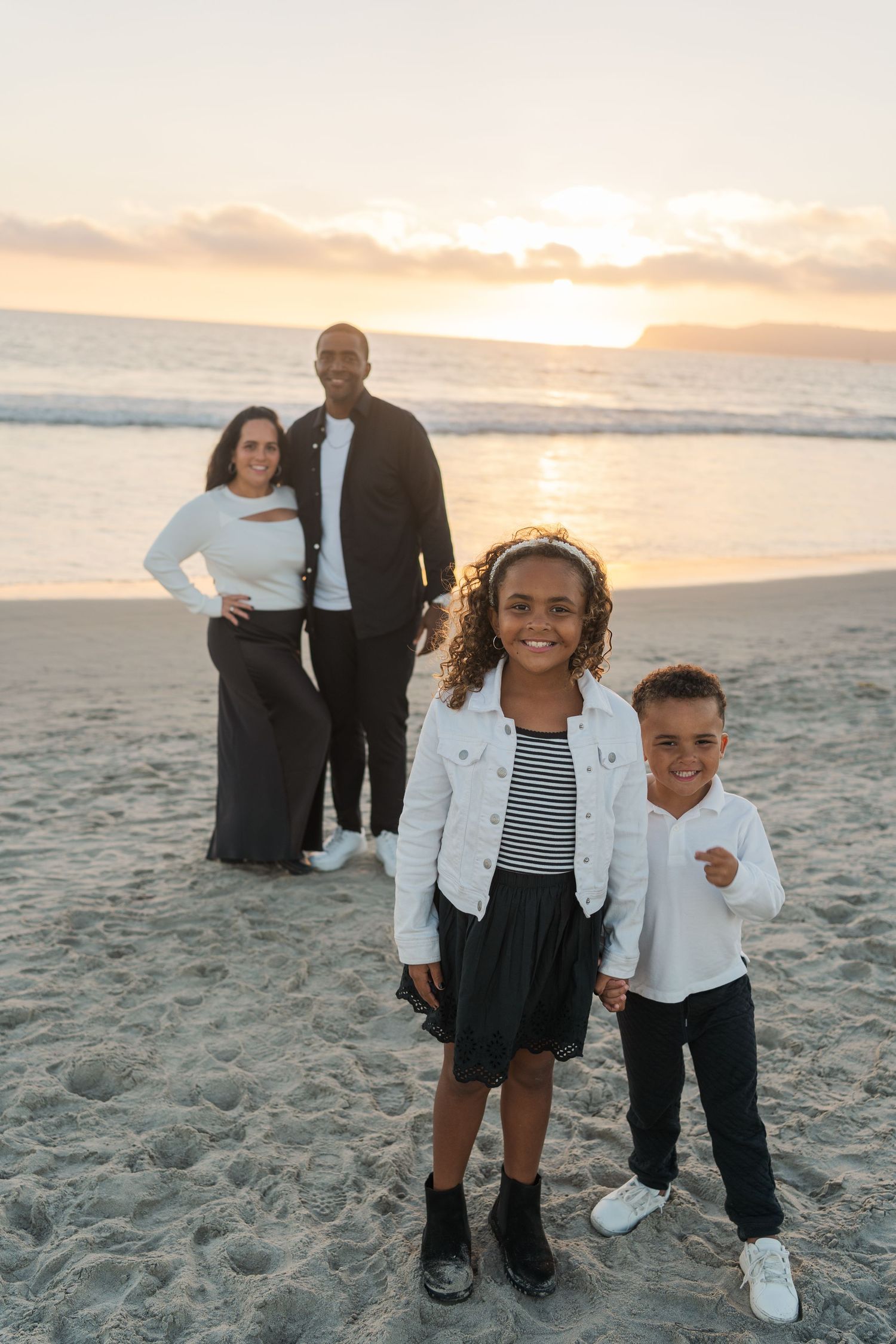A family poses together on a sandy beach during sunset with the ocean waves and glowing sky in the background.