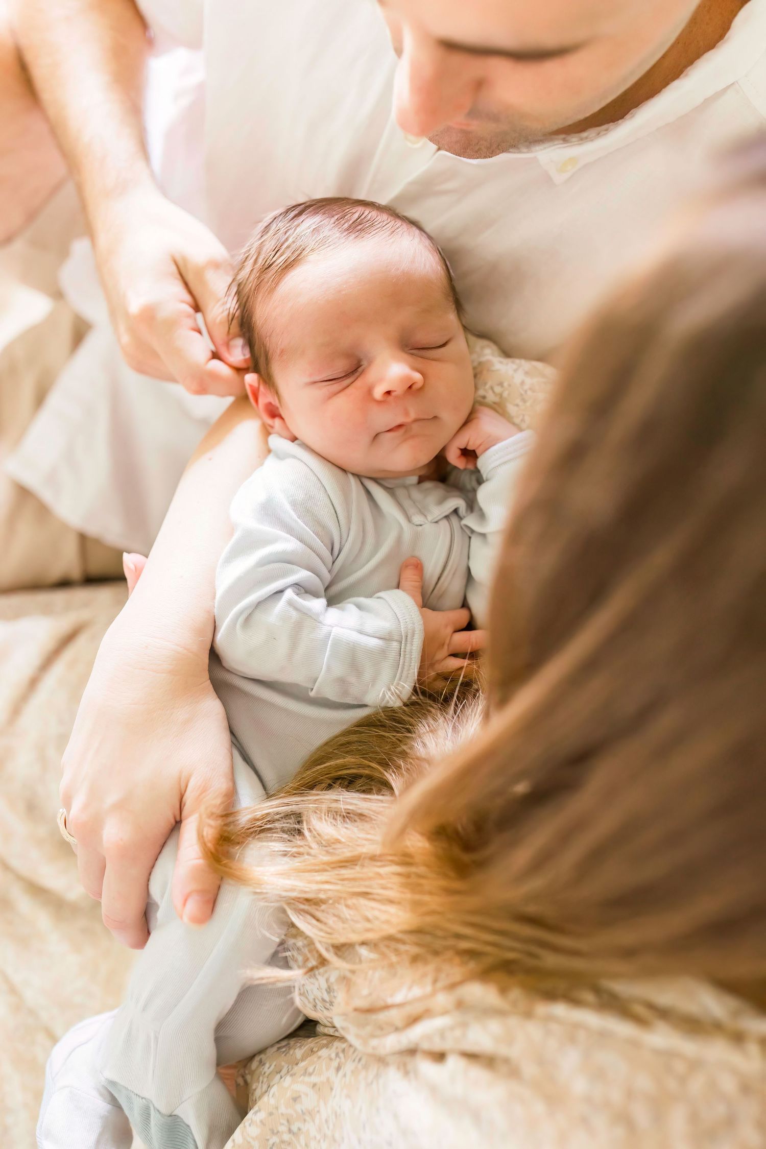 Close-up view of sleeping newborn being cradled in soft natural lighting.