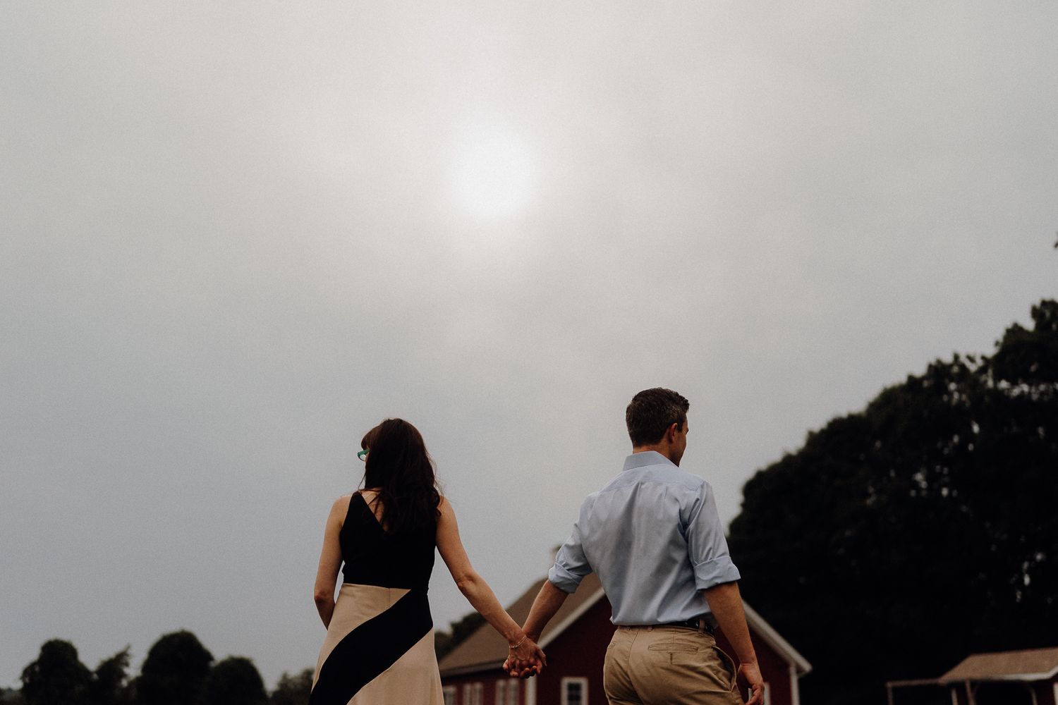 A silhouetted couple holding hands against a misty sky at sunset.