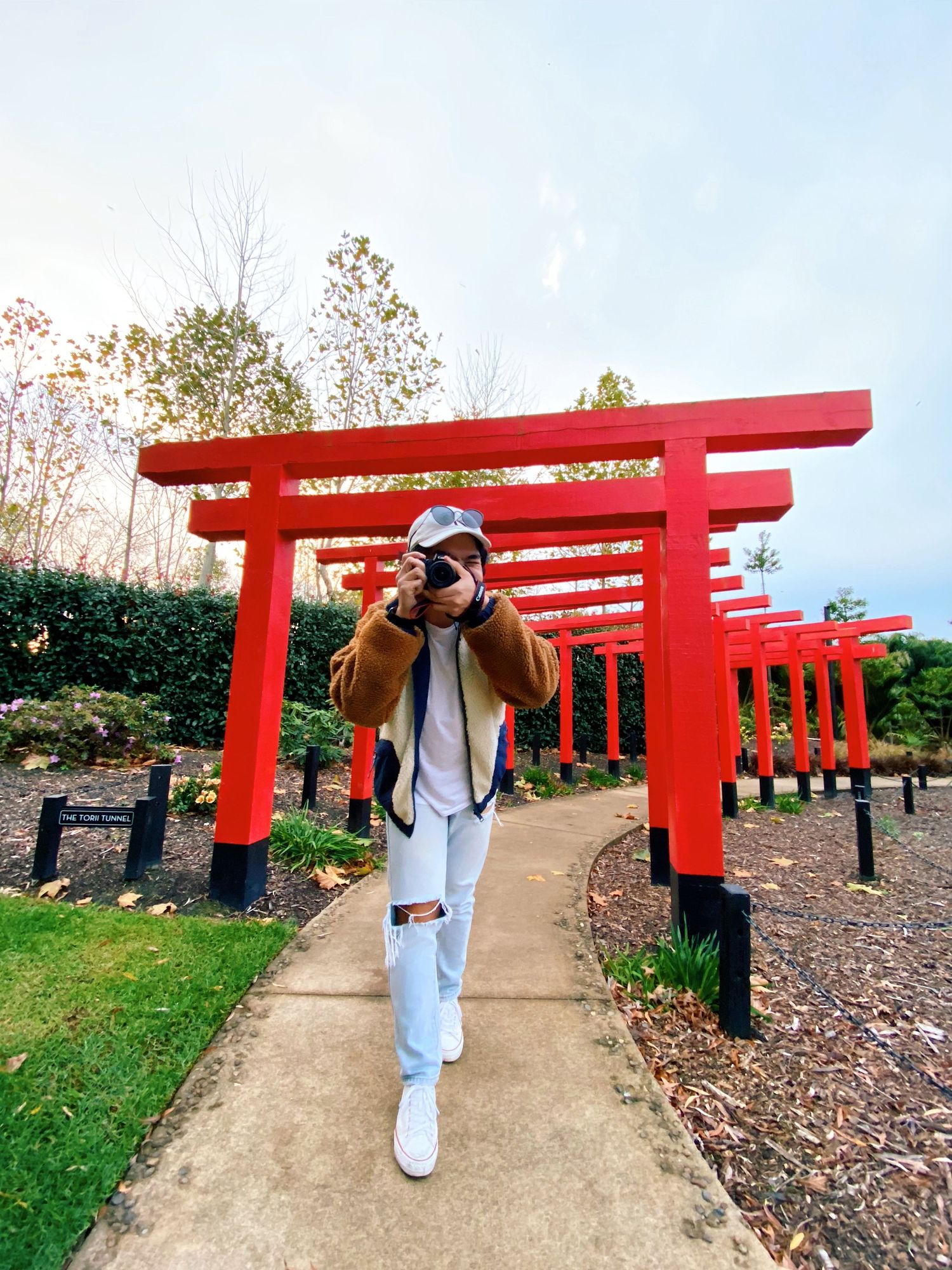 A path lined with traditional red torii gates at a Japanese shrine surrounded by autumn foliage.