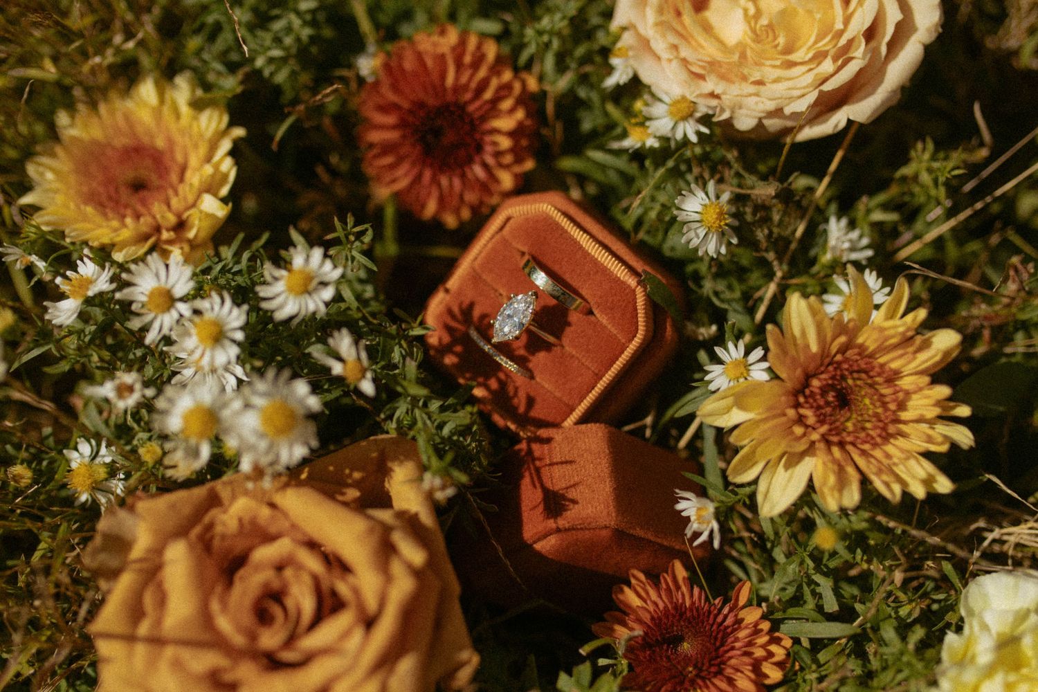 Diamond engagement ring in a velvet box surrounded by colorful autumn flowers including roses and daisies.