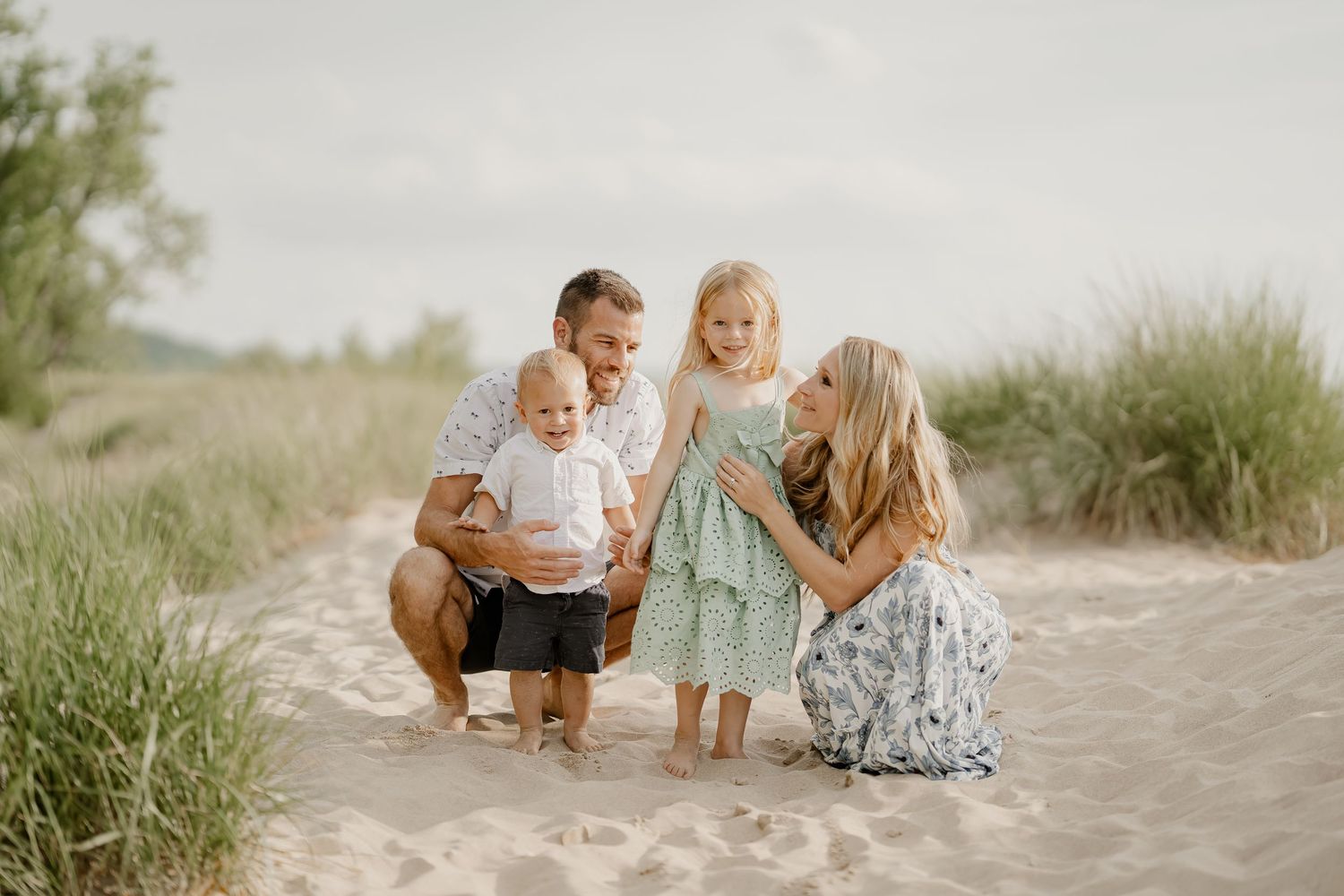 Family stands together in a golden wheat field during sunset.